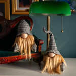 Load image into Gallery viewer, Two gnome figurines with plaid hats sitting on a wooden surface with a green lamp in the background.

