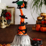 Load image into Gallery viewer, A decorative Halloween gnome, dressed in an orange outfit and wearing an orange hat adorned with bats, against a white background with books, pumpkins and a skull.
