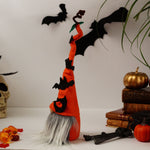 Load image into Gallery viewer, The side view decorative Halloween gnome, dressed in an orange outfit and wearing an orange hat adorned with bats, against a white background with books, pumpkins and a skull.
