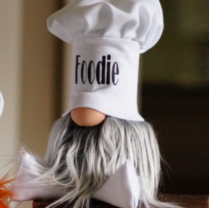 A handmade guardian, Chef Gnocchi gnome figurine with a foodie chef hat, long white beard, and round nose sits on a surface.