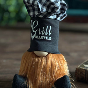 A gnome figurine with a long orange beard, Grill Master chef hat, and checkered top—Chef Gnocchi brings gourmet magic to your space.