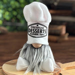 Load image into Gallery viewer, A plush gnome with a long gray beard and a large white chef hat that reads Premium Desserts Available Here sits on a round wooden cutting board. 
