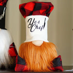 Load image into Gallery viewer, A close-up of a decorative gnome doll with a red and black buffalo plaid hat and matching hat on its head, a white face panel with the words 'Yes Chef!' in black script, and a bright orange beard. The gnome is sitting on a dark wooden surface against a soft beige background.

