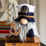 Load image into Gallery viewer, Handcrafted nautical captain gnome with a navy blue sailor hat and soft white beard, sitting on stack of books on a shelf as coastal beach house decor.
