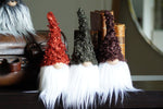 Load image into Gallery viewer, Four gnome figurines with different colored hair on a surface with books and a leather-bound box.
