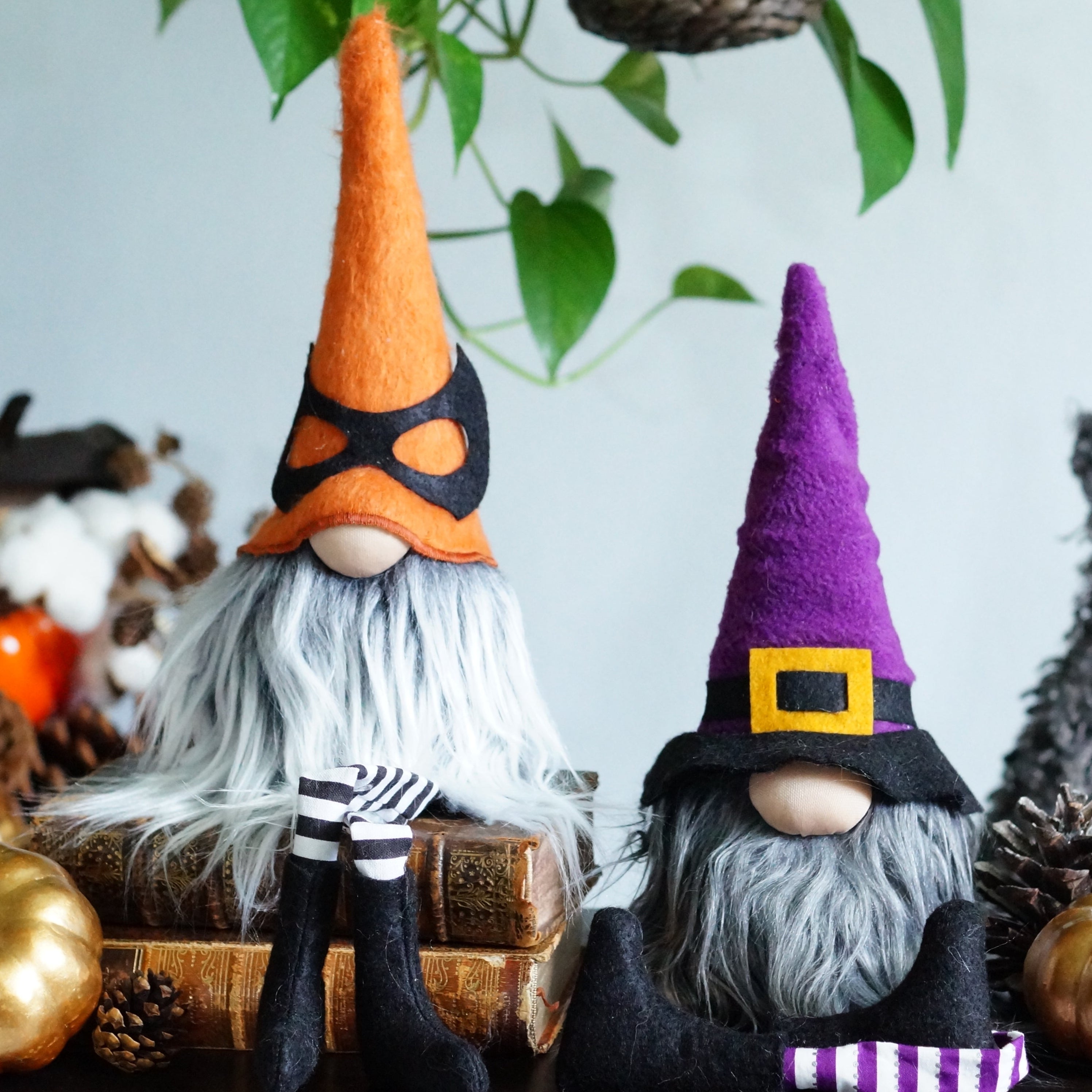 Two Halloween-themed gnomes with colorful hats on a table with pumpkins and decorations.