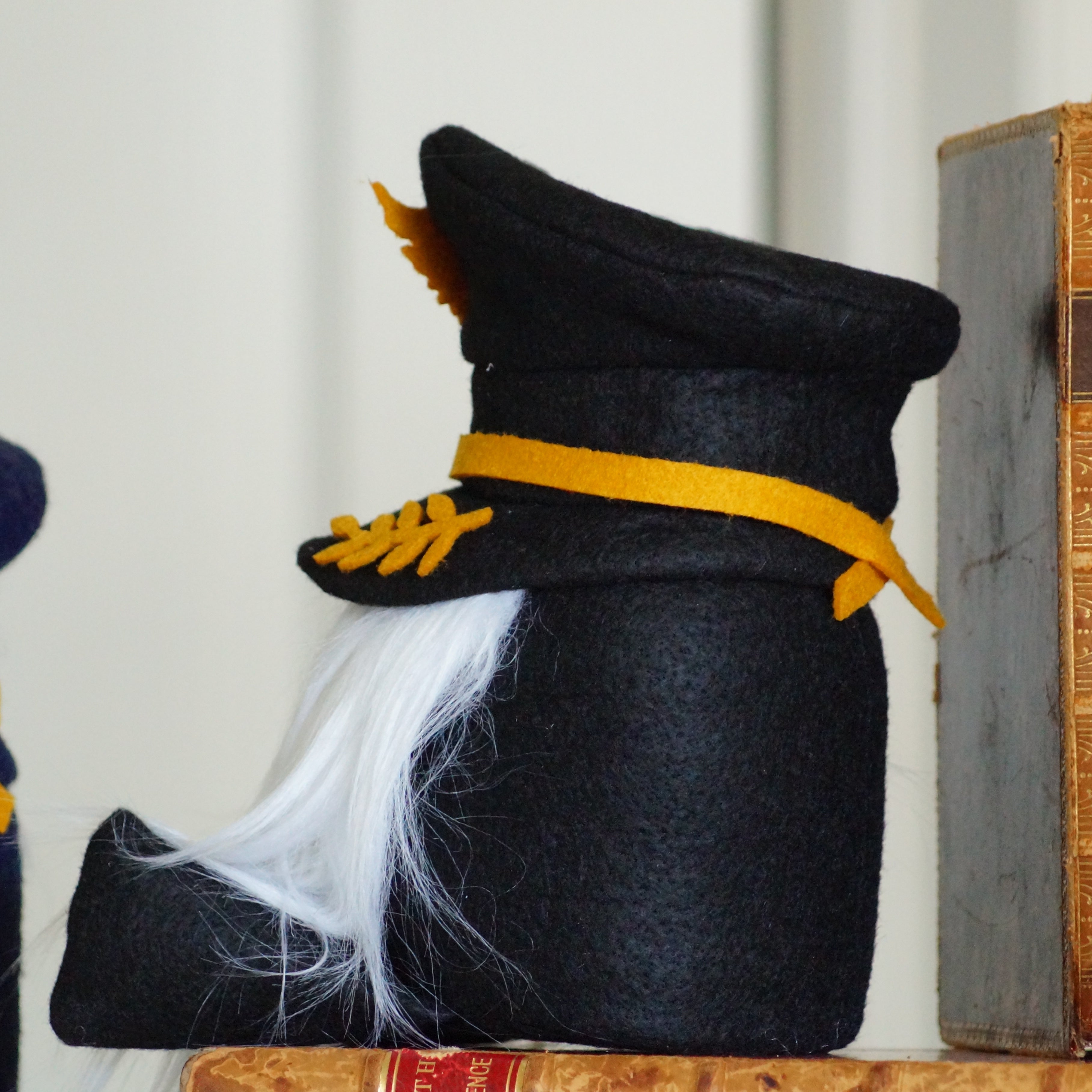 Decorative black hat with yellow band and white feather next to vintage books on a shelf.