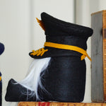 Load image into Gallery viewer, Decorative black hat with yellow band and white feather next to vintage books on a shelf.
