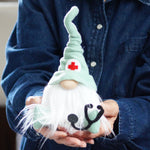 Load image into Gallery viewer, Person holding a plush gnome with a nurse hat and red cross symbol
