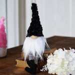 Load image into Gallery viewer, Decorative gnome with black hat and white beard on a wooden table with pastel-colored trees and a white flower arrangement.
