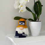 Load image into Gallery viewer, Small gnome figurine with a yellow hat and striped shirt next to white flowers on a light surface.
