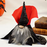 Load image into Gallery viewer, Dracula Halloween gnome with velvet black hat and cape with  gray beard, sitting on a white surface with books and a skull in the background. Ideal for cute Scandinavian Halloween tiered tray decor

