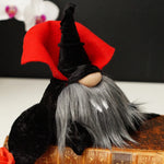 Load image into Gallery viewer, A Dracula Gnome with a black hat, red cape, and gray beard sits on a book. An enchanting indoor garden ornament with mysterious charm ideal for modern Halloween decor

