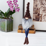 Load image into Gallery viewer, Gnome figurine with long hair and blue pants on a white surface with a plant and books in the background.
