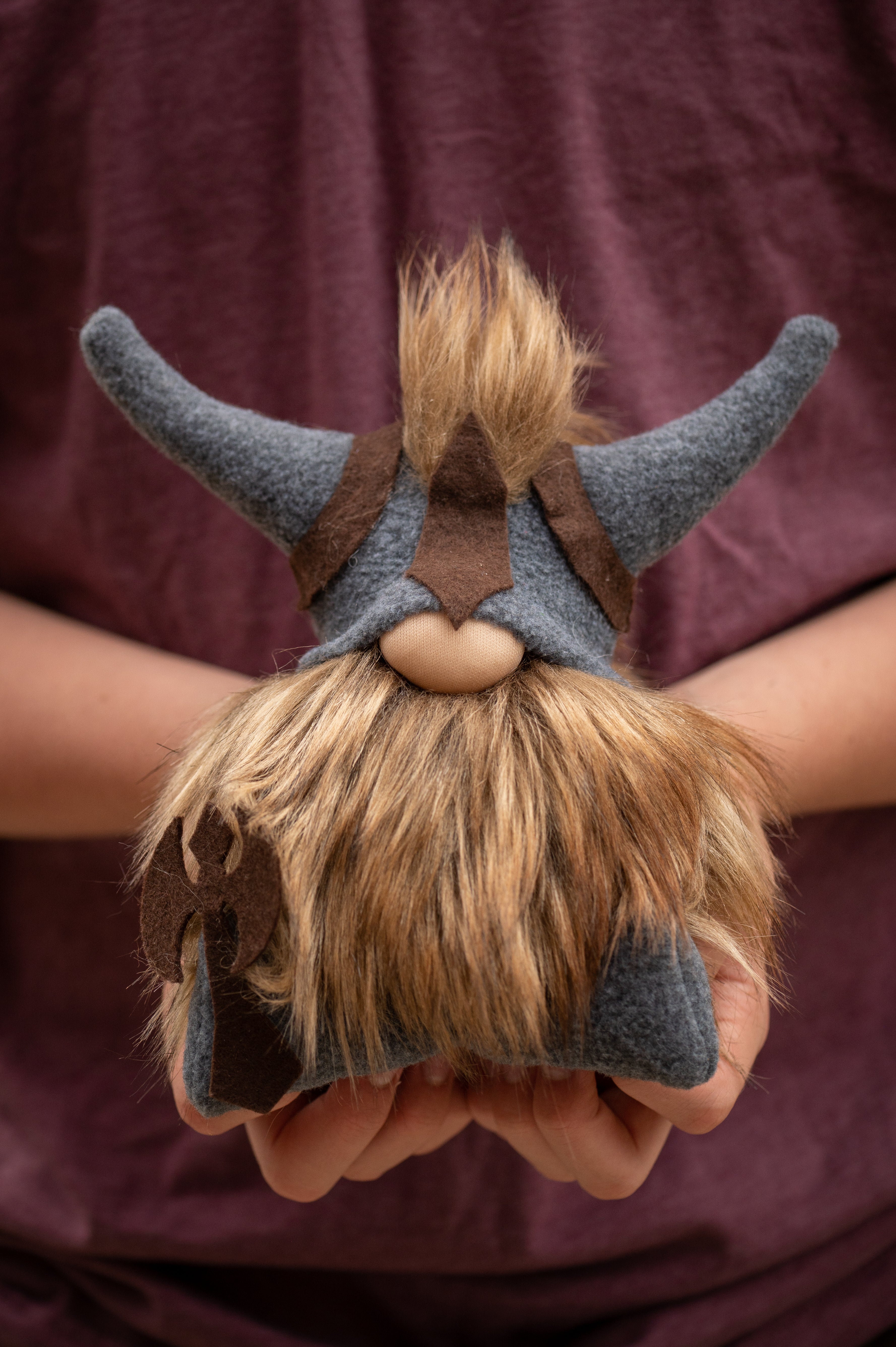 A person holds Gimli the Viking, a handmade plush gnome with a horned helmet, faux fur beard, and an axe on its side.