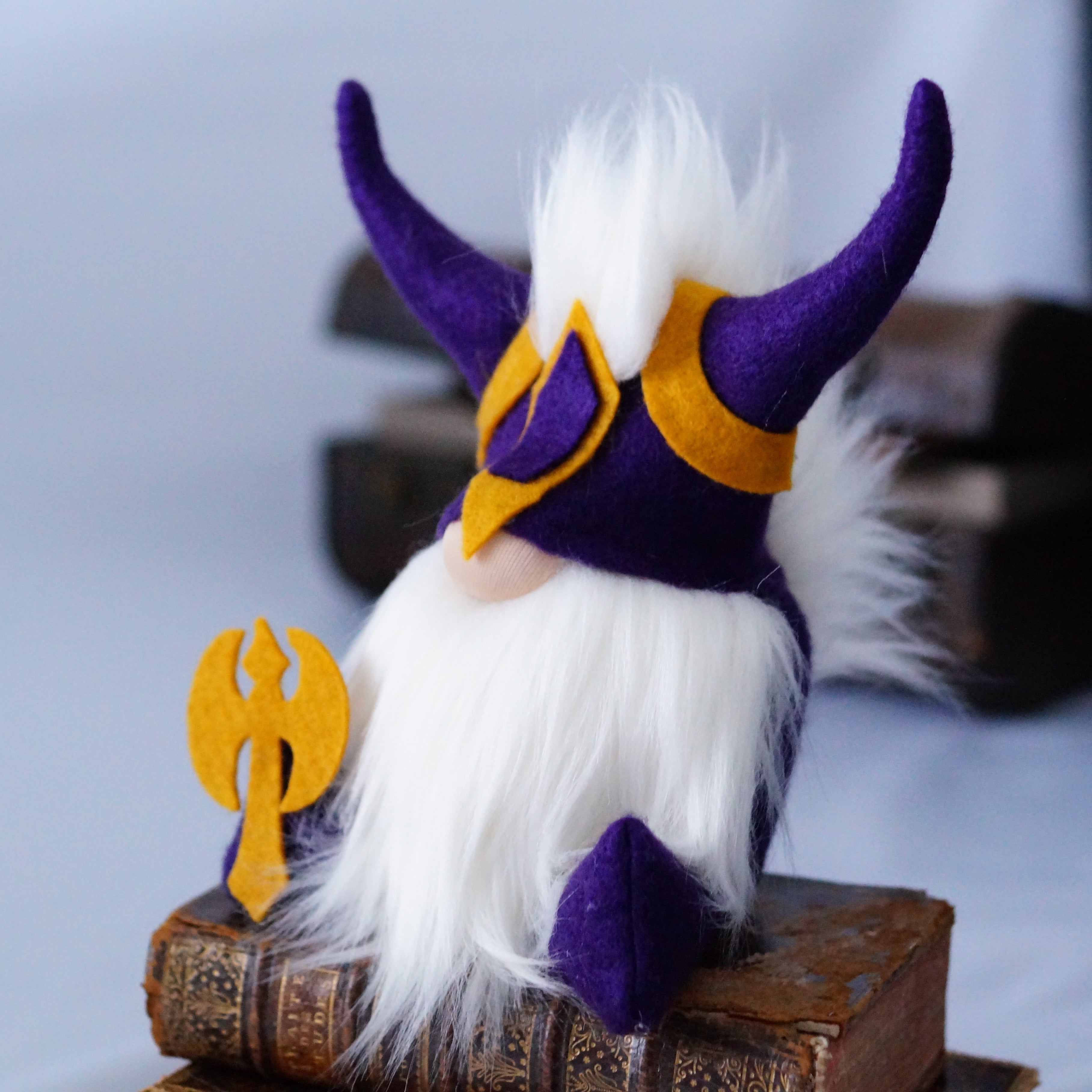 A handmade focus guardian plush, featuring purple horns, white fur, and gold armour, rests on old books—perfect for those looking to achieve their goals.
