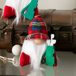 Load image into Gallery viewer, Two gnome figurines with plaid hats and green scarves on a reflective surface with a vintage suitcase in the background.
