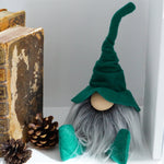 Load image into Gallery viewer, Gnome figurine with green hat and gray beard on a shelf with books and pinecones.
