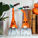 Load image into Gallery viewer, Two Halloween-themed gnomes with orange hats and black eyes on a shelf with pumpkins and books.
