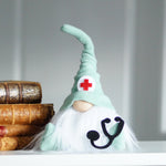 Load image into Gallery viewer, Doctor gnome figurine featuring a stethoscope and red cross, displayed on a table next to books.
