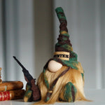 Load image into Gallery viewer, Gnome figurine with green and brown camouflage outfit hat and 'HUNTER' band, holding a rifle, on a white surface with books in the background.
