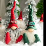 Load image into Gallery viewer, Two handmade holiday guardians, Naughty in red and Nice in green, sit bearded in snowy hats with trees in the background.
