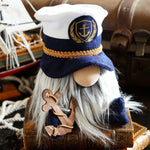 Load image into Gallery viewer, A gnome wearing a nautical captain's hat with a anchor emblem, sitting beside a miniature sailboat.
