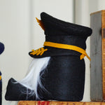 Load image into Gallery viewer, Decorative black hat with yellow band and white feather next to vintage books on a shelf.
