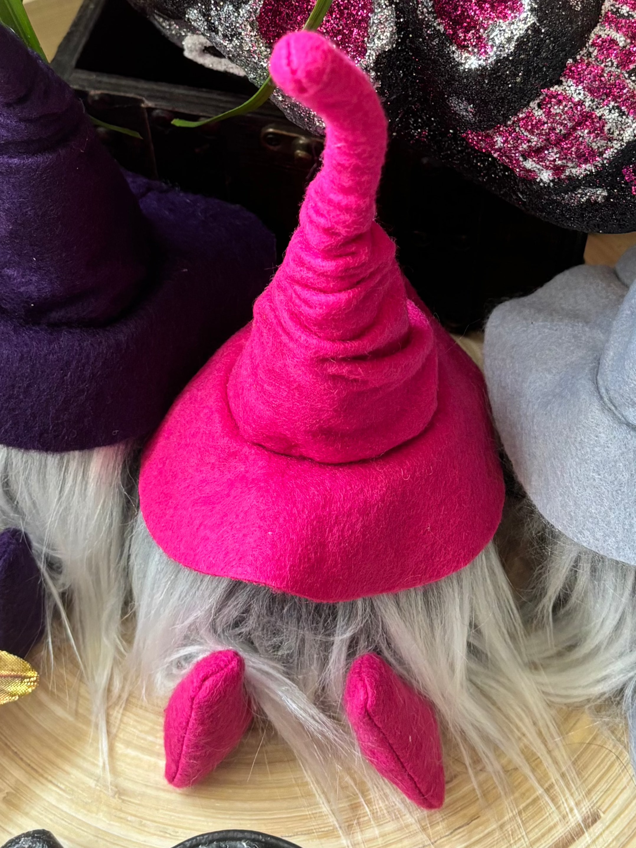 A small gnome with a tall pink hat, gray beard, and pink shoes sits on a woven mat—an ideal handmade library guardian for your study or home office.
