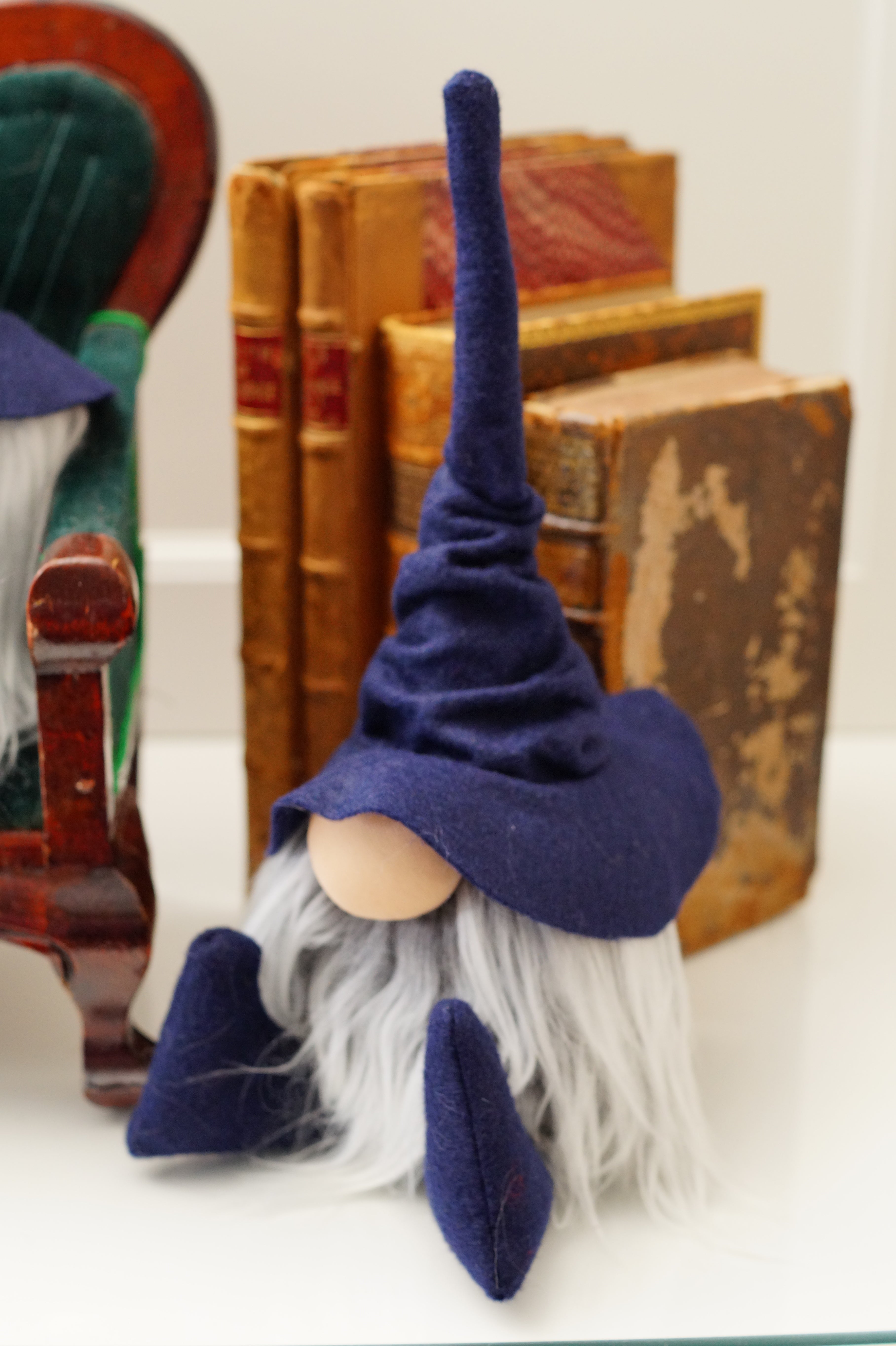 A small gnome figurine with a tall blue hat and long white beard sits by old books—a charming handmade library guardian for your study or home office.
