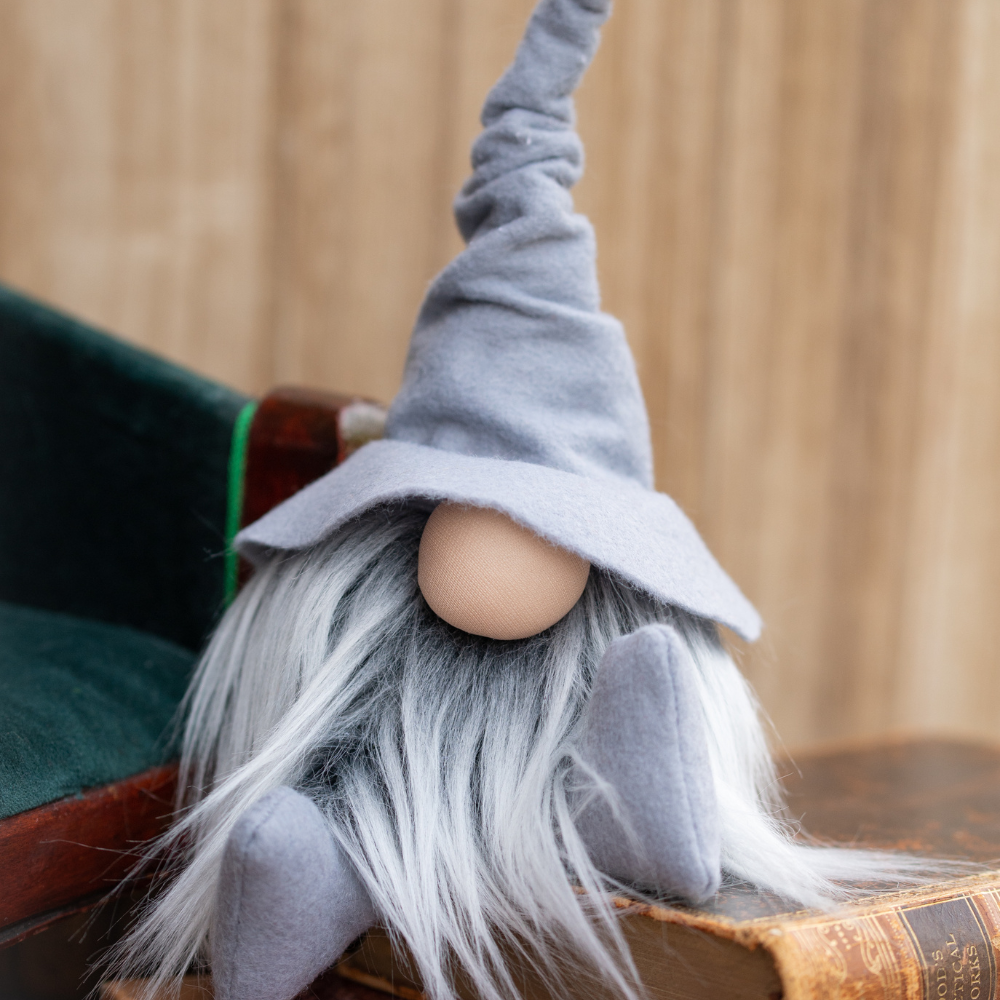 A handmade gnome doll with a long gray beard and tall hat sits on old books, making a charming library guardian against a wooden background.