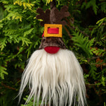 Load image into Gallery viewer, A decorative gnome ornament with a brown body, red hat, and a white beard hanging from a branch in a green outdoor setting.
