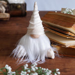 Load image into Gallery viewer, Small gnome figurine with white beard on a wooden surface with books and flowers.
