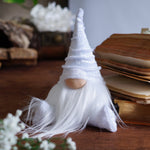Load image into Gallery viewer, White gnome figurine with a beard on a wooden surface with books and flowers.

