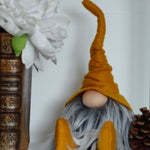 Load image into Gallery viewer, Gnome figurine with a mustard hat and gray beard next to books and a pine cone on a white surface.
