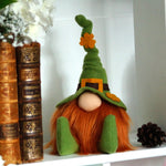 Load image into Gallery viewer, The Irish Lad, a St. Patrick's Day decorative gnome with a pointy bendable green hat, sitting on a wooden shelf next to books.

