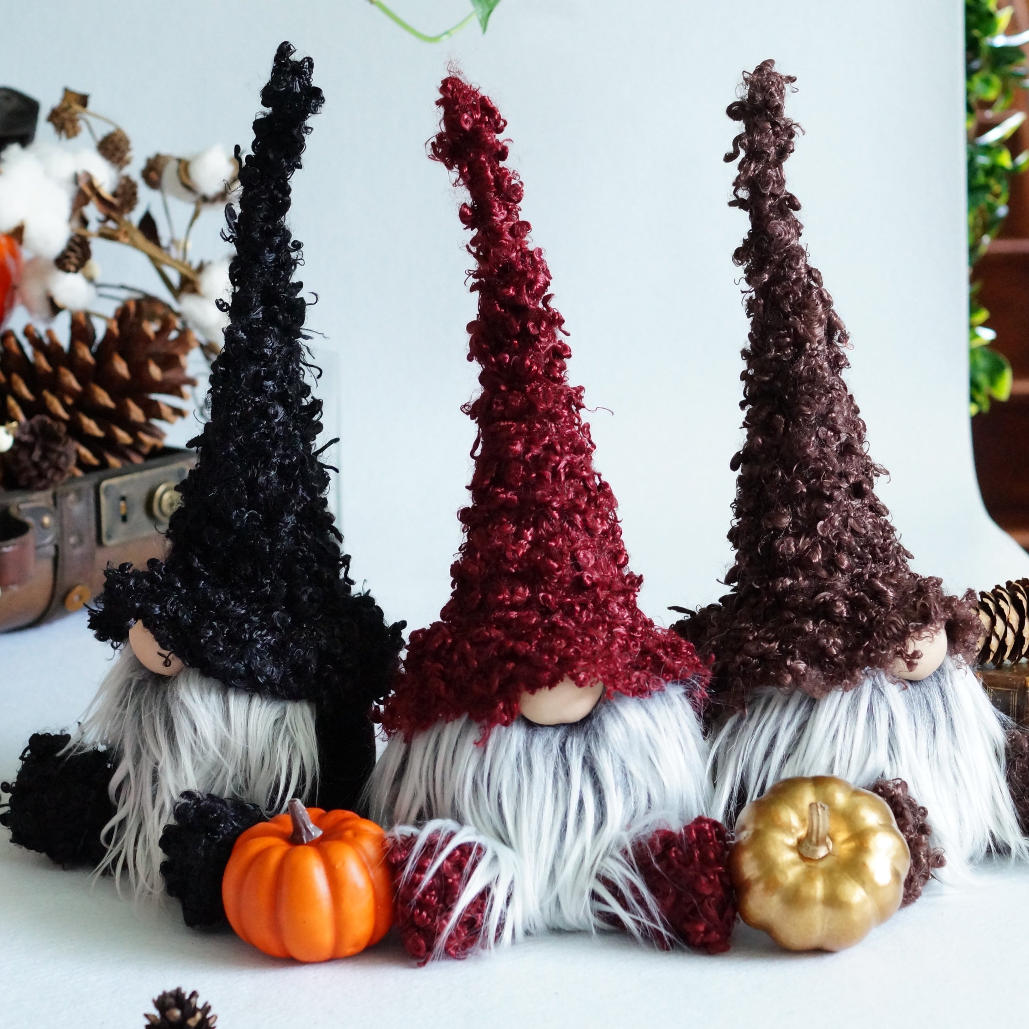 Three decorative gnomes with autumn-themed accessories on a table.