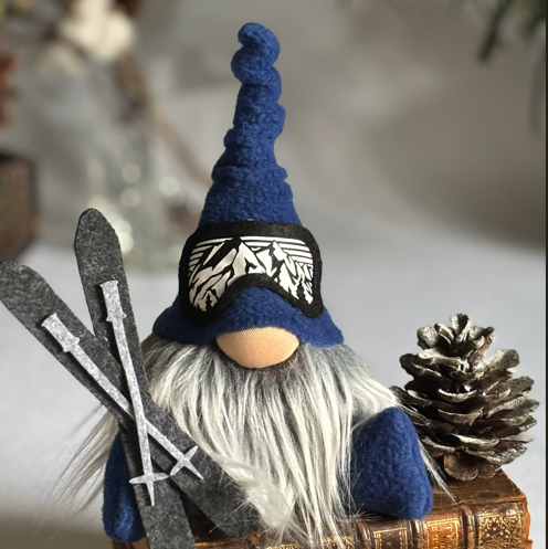 Gnome figurine with blue hat and beard, holding skis and a pine cone, on a book.
