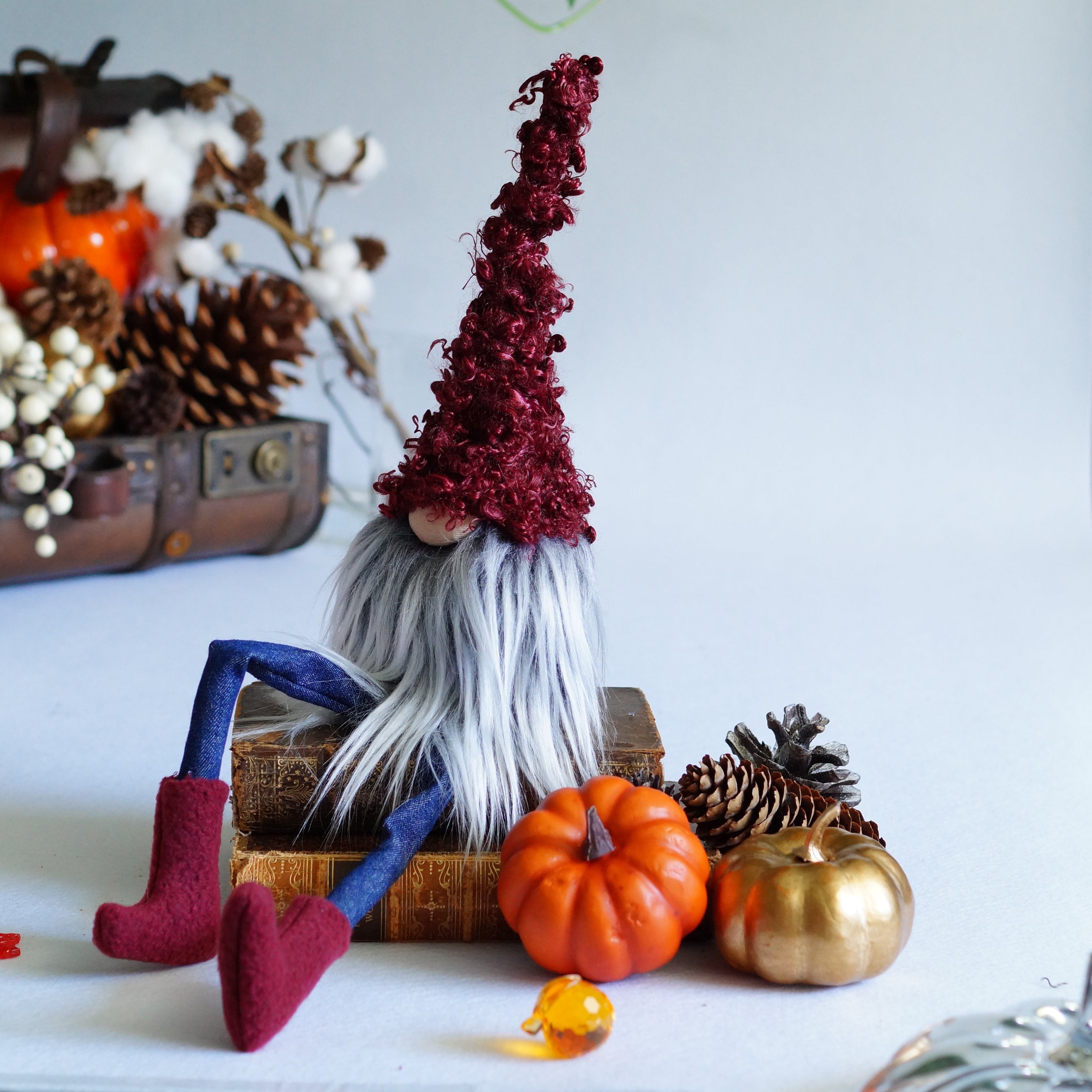 Decorative setup with a gnome, pumpkins, and pinecones on a white surface.