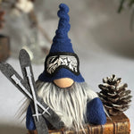 Load image into Gallery viewer, Gnome figurine with a blue hat and skis and goggles on a stack of books with a pine cone in the background.
