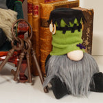 Load image into Gallery viewer, A handmade gnome with a green head resembling Frankenstein's monster, with a black patch over one eye and a wooden screw on the hat. The gnome has a gray beard and is seated against a decorative  background. Ideal for cute Halloween decor
