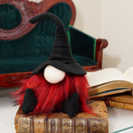 Load image into Gallery viewer, A handmade fall gnome doll with red hair and a black hat sits on vintage books beside a green velvet chair—perfect Halloween decorations.

